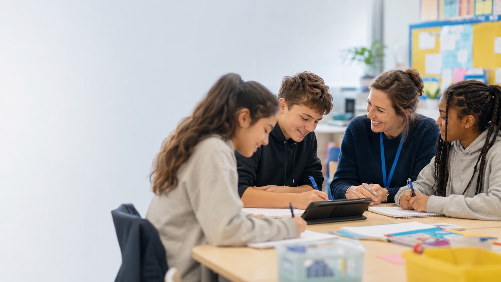 A worker sitting alongside young people at a table, smiling over a tablet